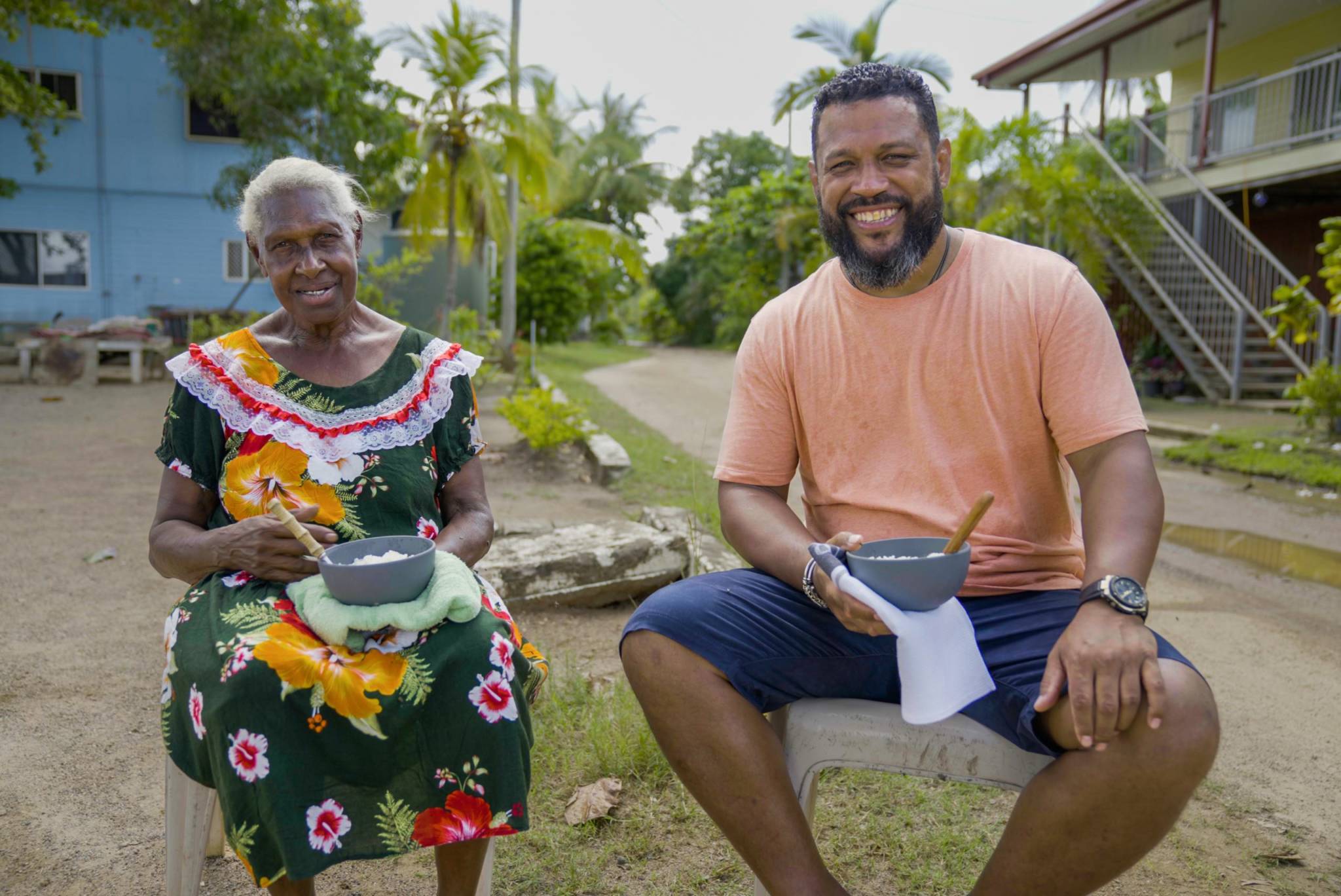 Aaron Fa'Aoso sits outside next to a woman with pots in their hands as part of series STRAIT TO THE PLATE