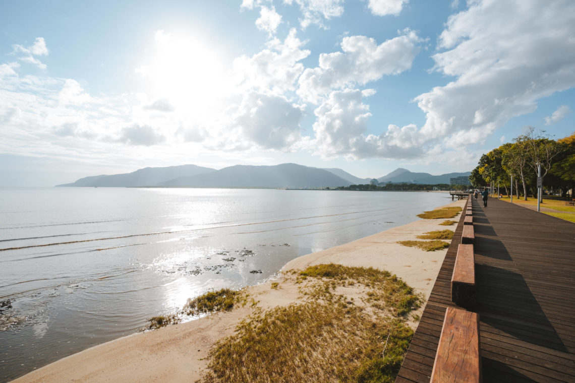 A photograph of the esplanade in Cairns showing sand, ocean and hills