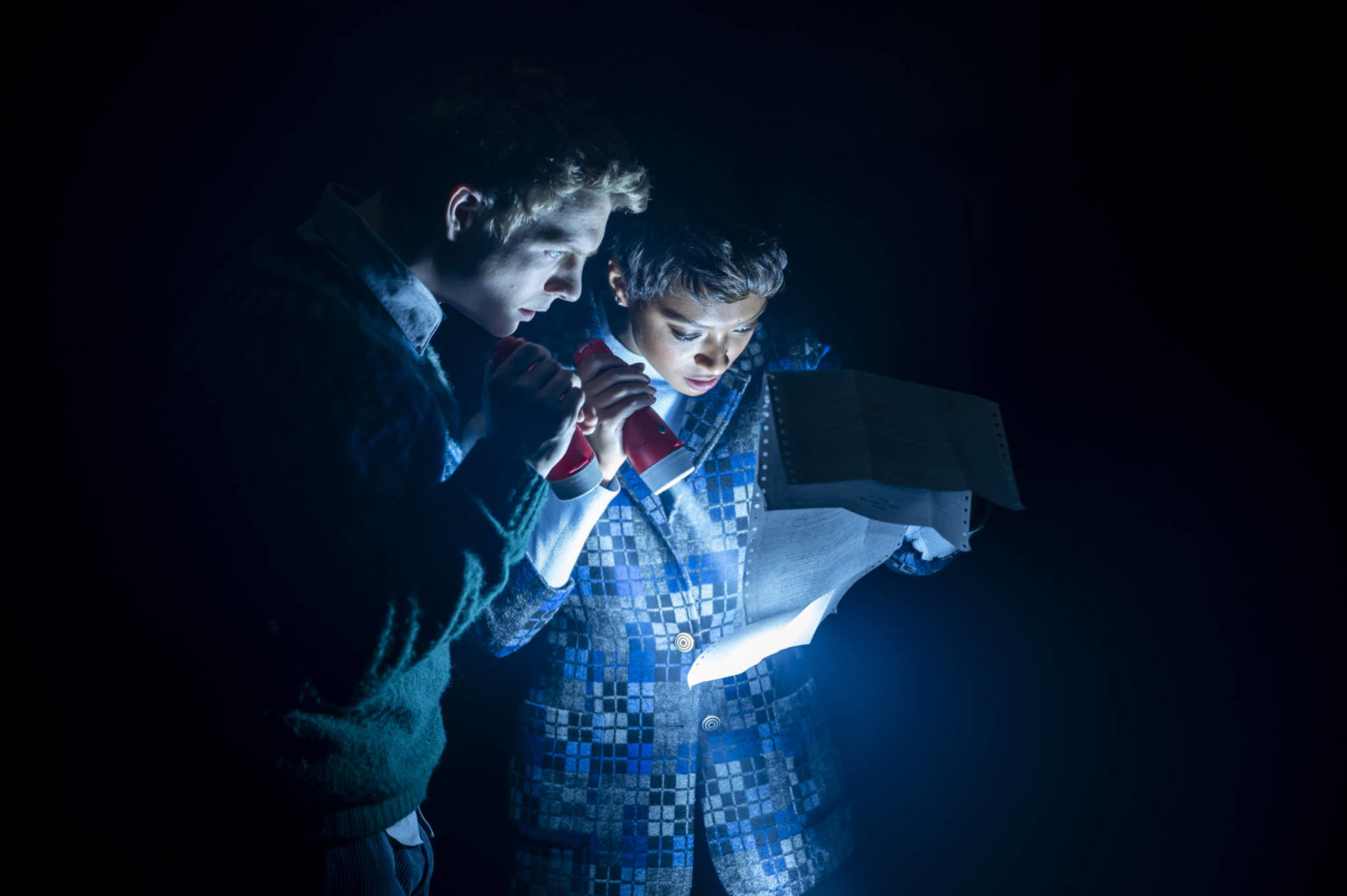Paul Carpenter (Patrick Gibson) and Sophie Pettingel (Sophie Wilde) together in the darkness of The Bank Of The Dead reviewing a letter with a torch