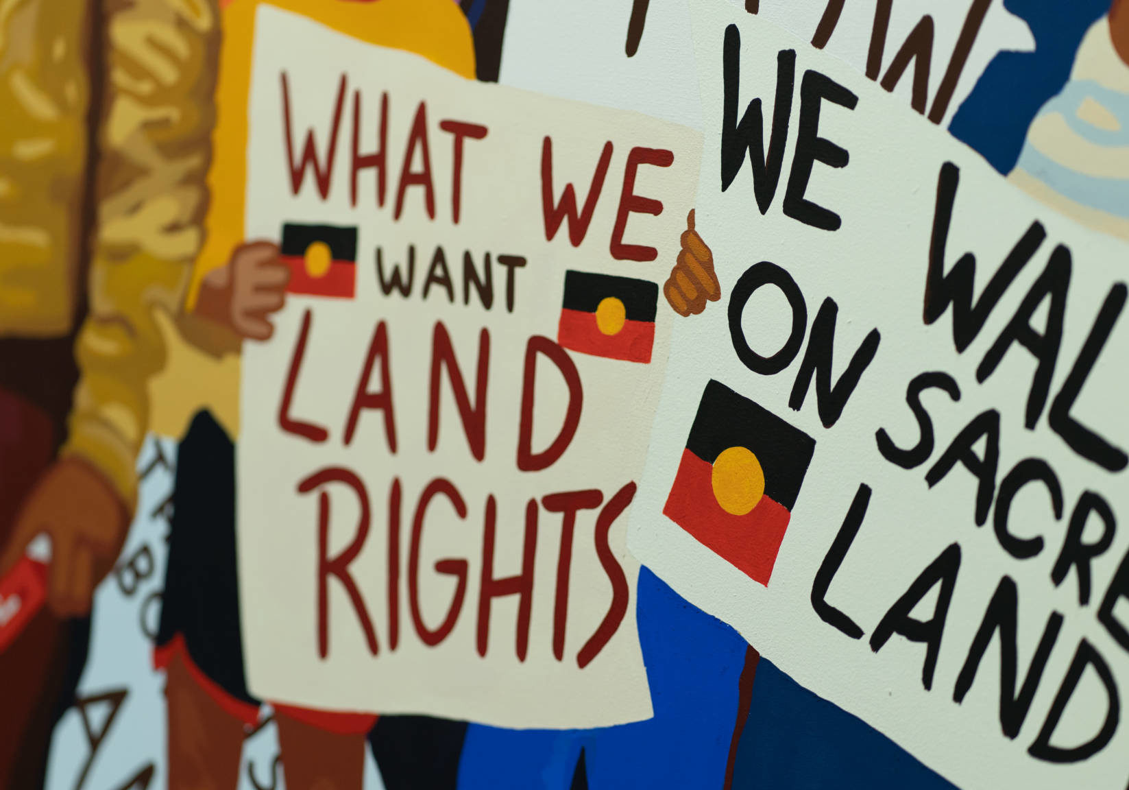 A painting of people holding signs that say "What we want: Land Rights" and "We walk on sacred Land" from the documentary YOU CAN GO NOW