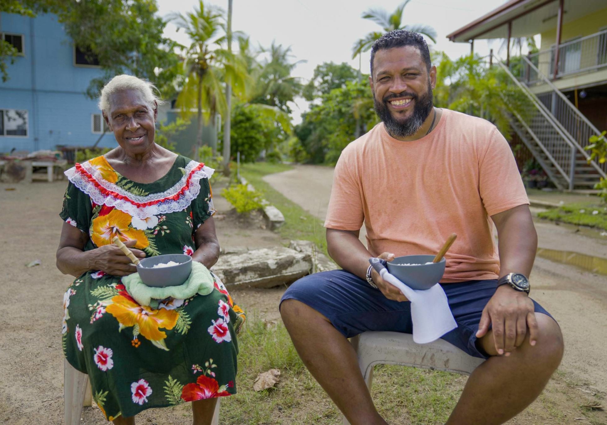 Aaron Fa'Aoso sits outside next to a woman with pots in their hands as part of series STRAIT TO THE PLATE