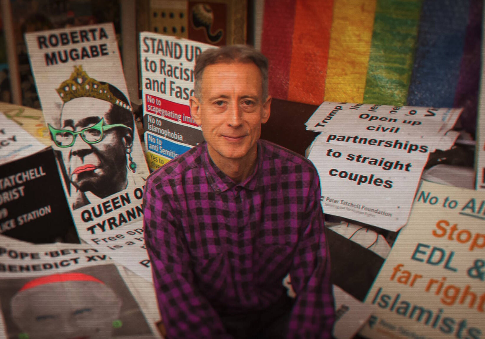 A still from HATING PETER TATCHELL of Peter Tatchell in front of signage and a rainbow flag