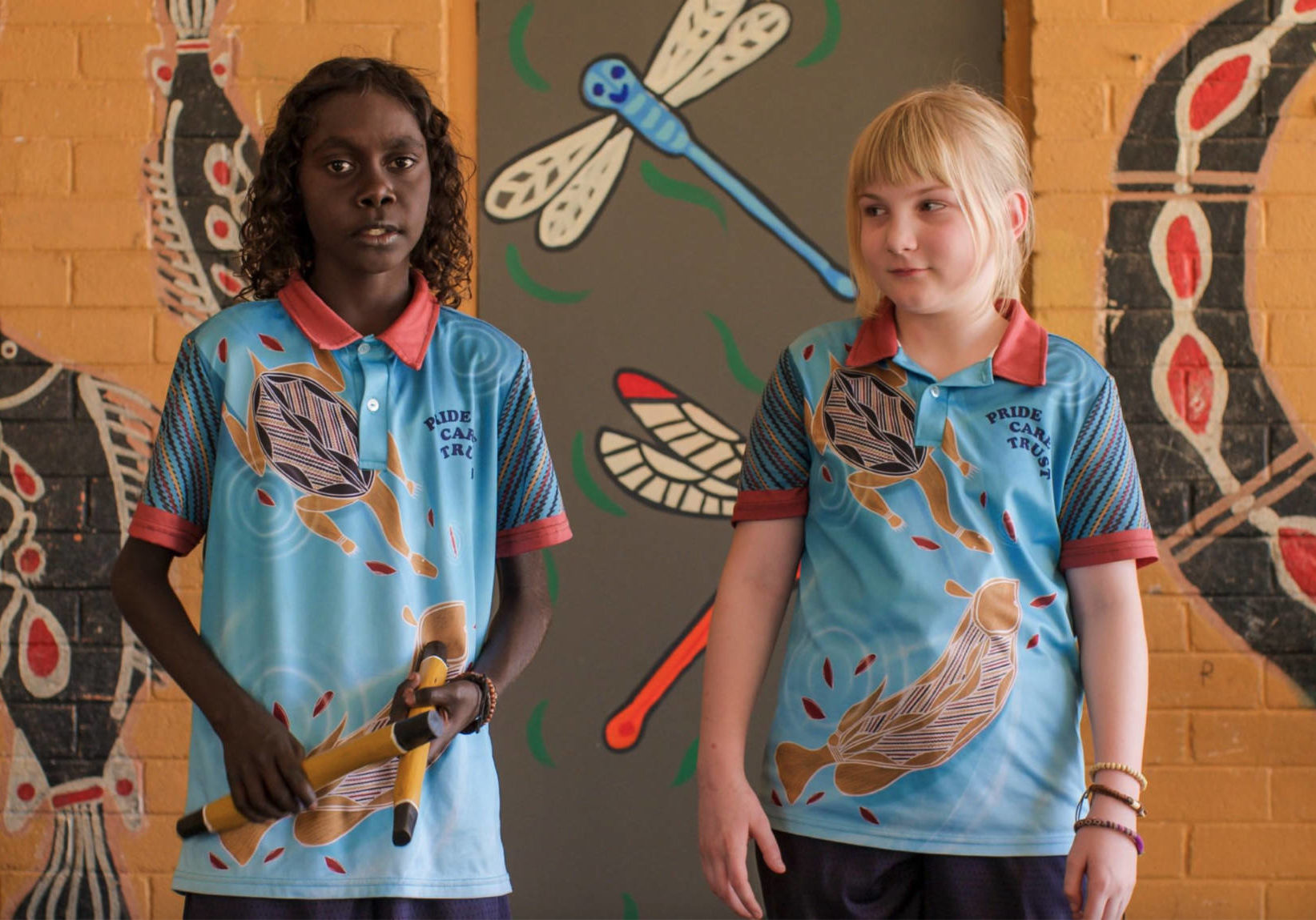 A photo of two children in school uniforms with colourful artwork behind them