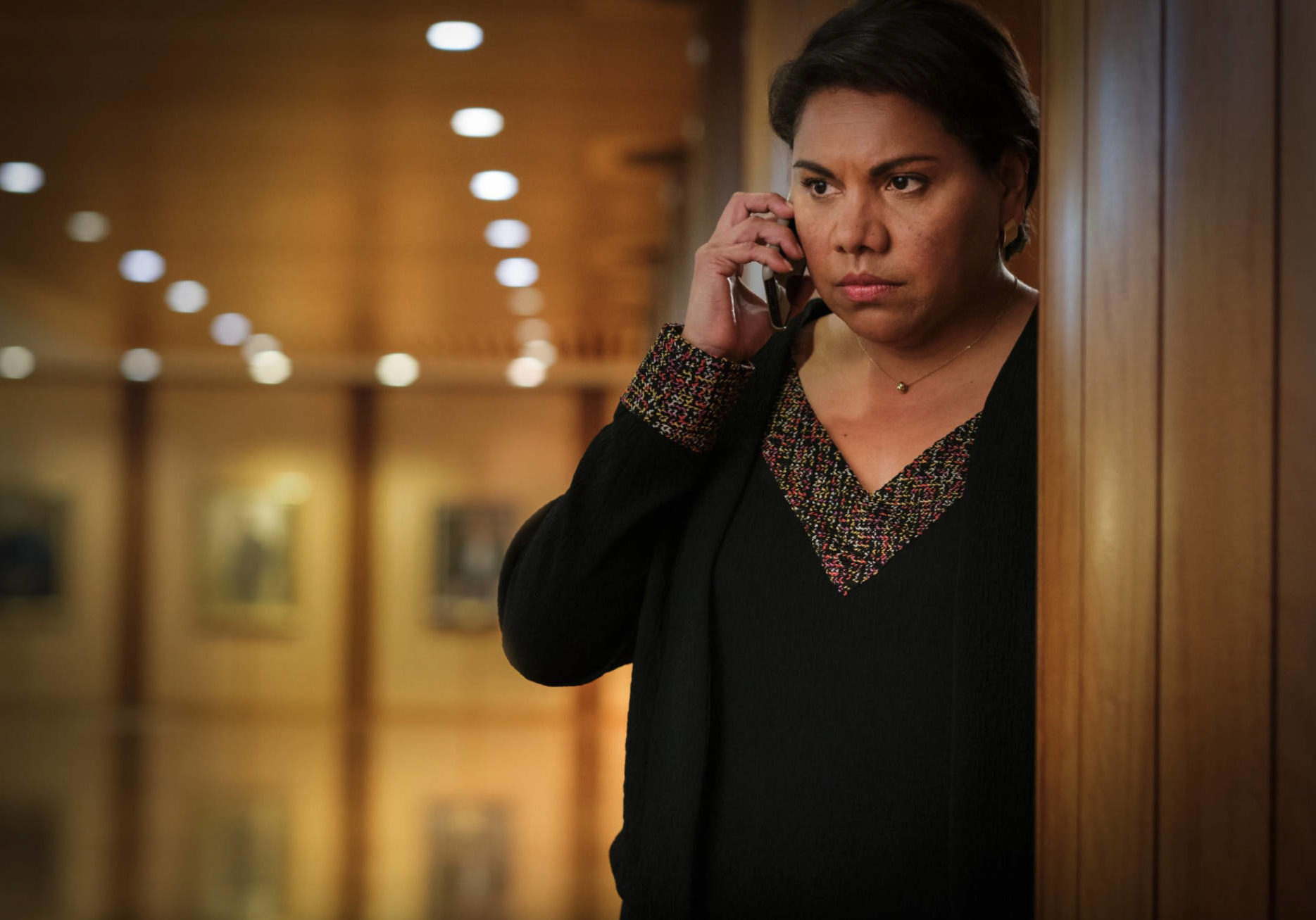 Deborah Mailman plays Alex Irving in TOTAL CONTROL. In the image she is looking series while on a phone call in a corridor