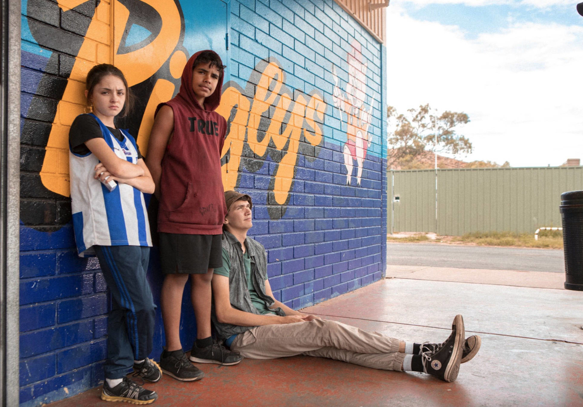A photo of three young people leaning against a colourful brick wall outside from the series ROBBIE HOOD