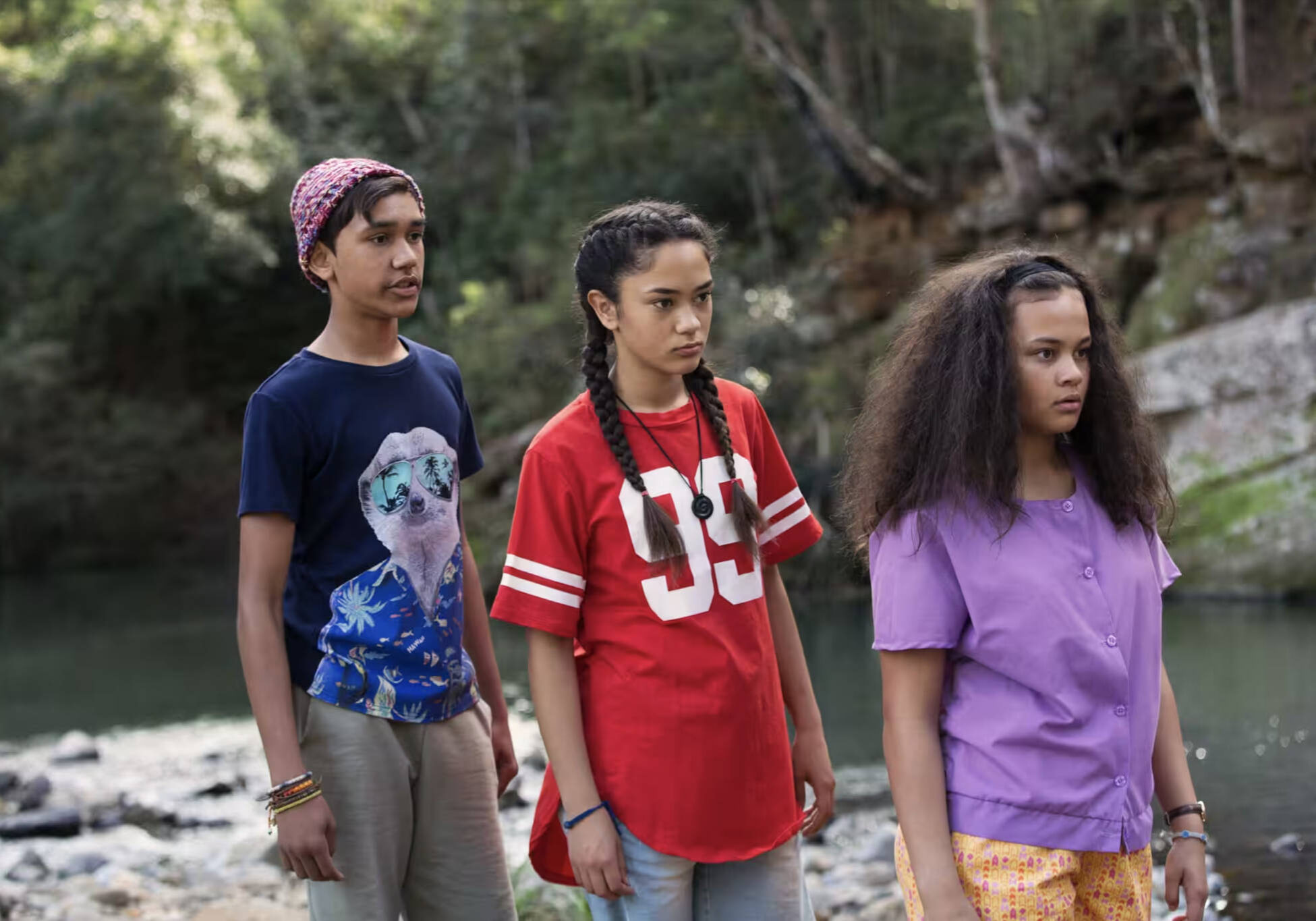 Three young people stand behind one another near a creek in GRACE BESIDE ME